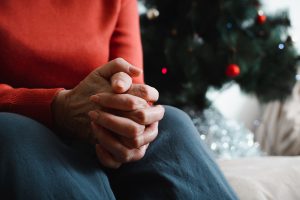 Lonely senior woman sitting at home in Christmas celebration. Close-up of an elderly woman's hand against background of decorated Christmas tree. 
