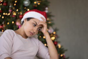 Woman in Santa hat looking frustrated in front of Christmas tree.