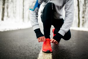 Young male runner preparing his sneakers for running. Tying shoelaces on a snowy road.
