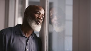 A man with a sad expression staring out a window.